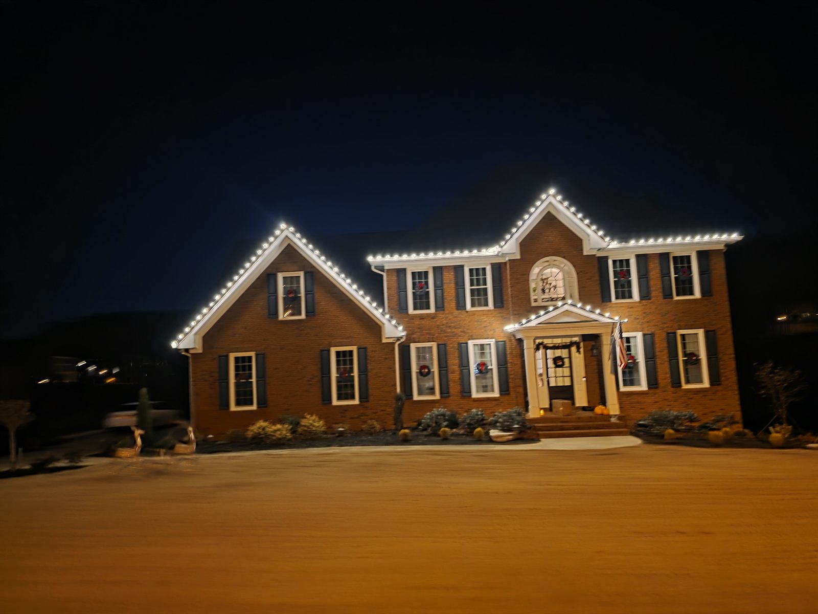 Completed nighttime installation on a two-story brick house, with white lights along the roofline and porch