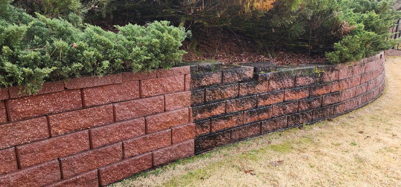 Red block retaining wall partly cleaned: the left section is bright red, the right section is still dark with grime