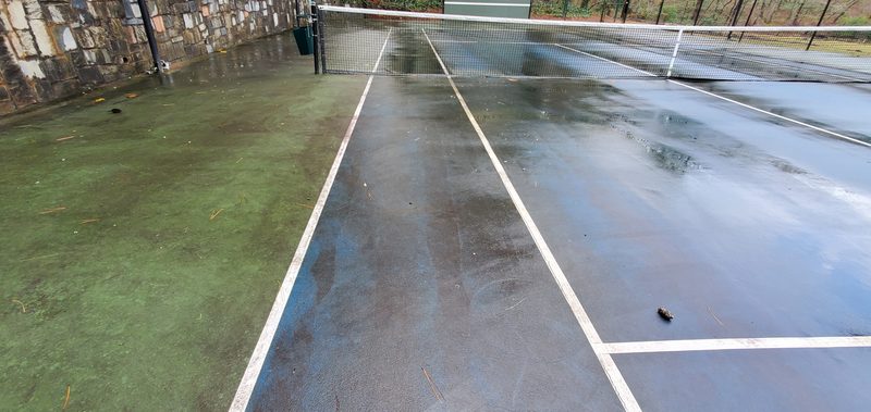 Tennis court surface covered in green and dark grime before cleaning