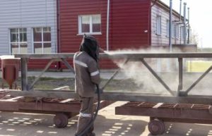 A worker in special clothing sandblasting a metal building structure.