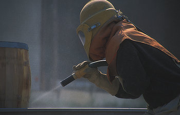 worker surrounded by flying debris sandblasting wooden barrel preparing it for use